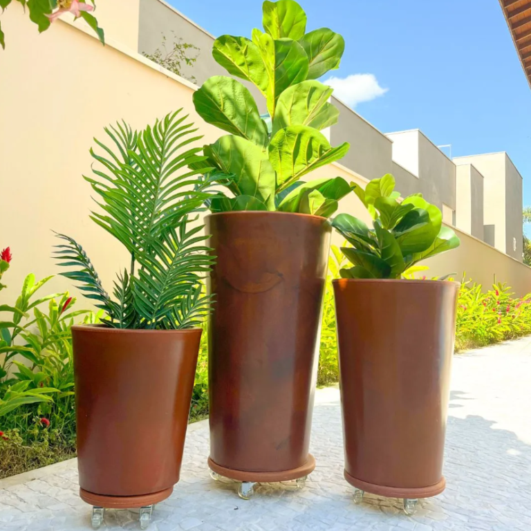 Três vasos altos marrons com plantas sobre rodízios