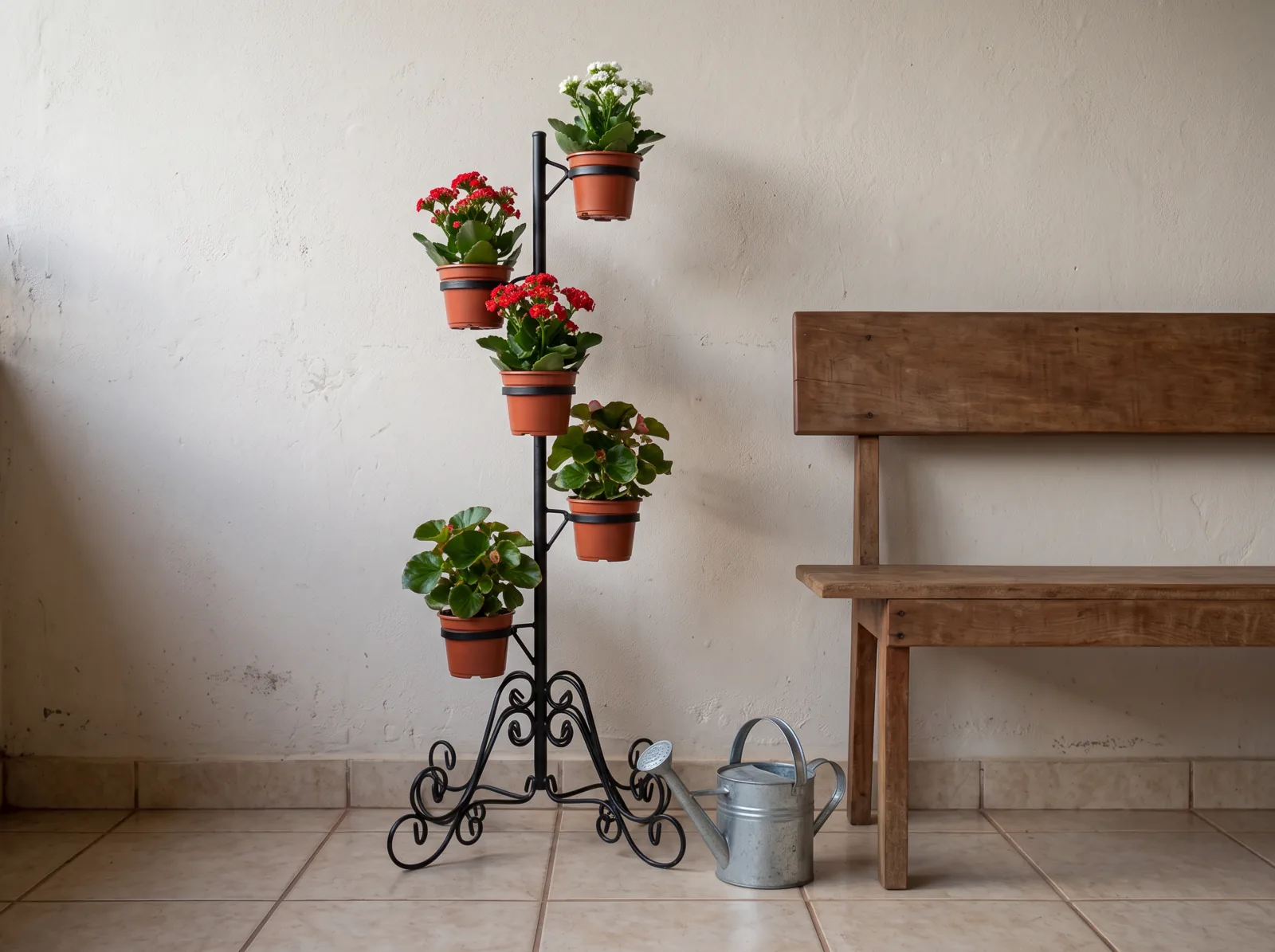 Suporte de chão em ferro preto com 5 vasos pequenos montado como árvore de Natal viva, com begônias embaixo, kalanchoes vermelhos no meio e kalanchoe branco no topo, ao lado de um banco na varanda